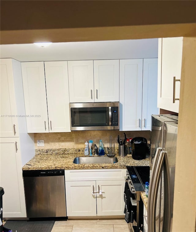 kitchen with sink, tasteful backsplash, light stone counters, white cabinets, and appliances with stainless steel finishes