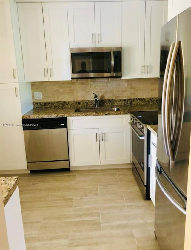 kitchen with appliances with stainless steel finishes, backsplash, sink, dark stone countertops, and white cabinets