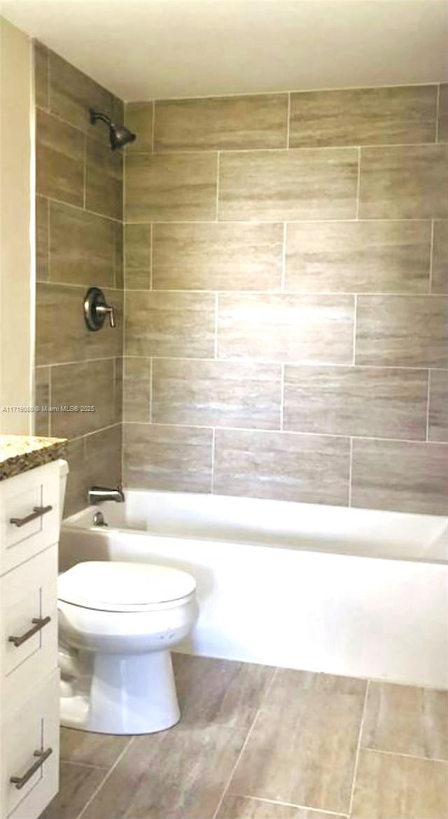 full bathroom featuring tiled shower / bath, vanity, and toilet