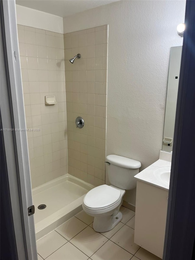 bathroom with a tile shower, tile patterned flooring, vanity, and toilet