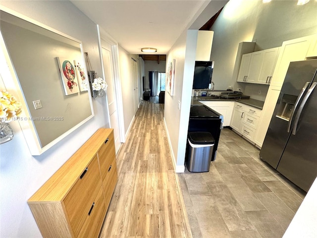 kitchen featuring baseboards, light wood-style floors, white cabinets, dark countertops, and stainless steel fridge