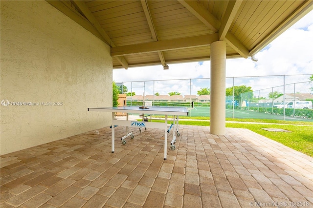 view of patio with a tennis court and fence