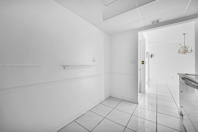 tiled spare room featuring a paneled ceiling and a notable chandelier