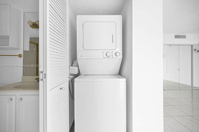 clothes washing area with sink, stacked washing maching and dryer, a textured ceiling, and light tile patterned floors