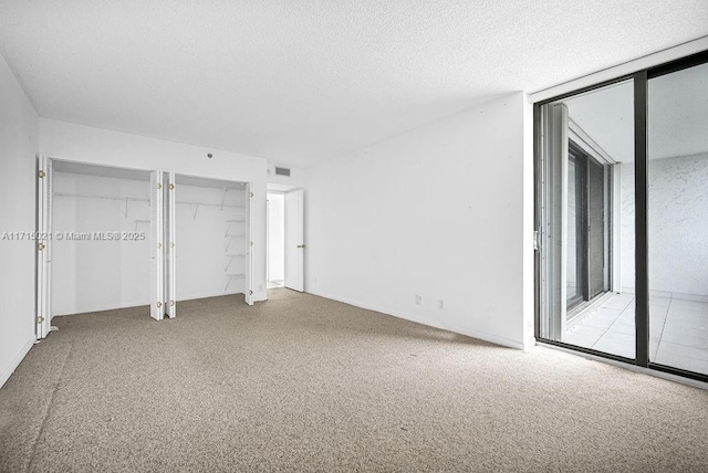 unfurnished bedroom with light carpet, a textured ceiling, access to outside, and floor to ceiling windows