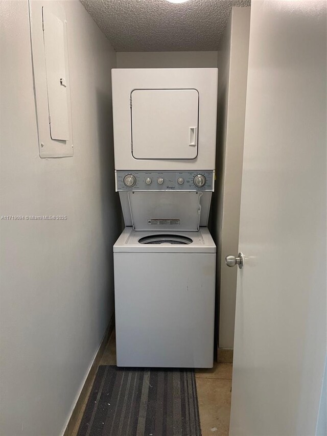 clothes washing area with a textured ceiling, electric panel, and stacked washer and clothes dryer