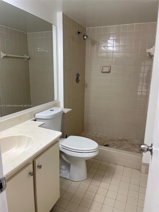 bathroom with tile patterned flooring, a tile shower, vanity, and toilet