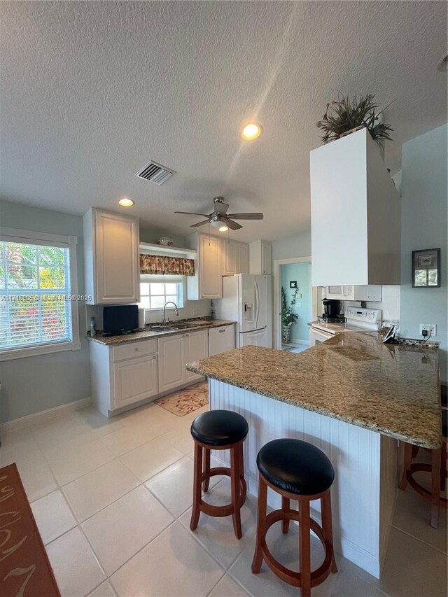 kitchen with kitchen peninsula, a kitchen bar, white appliances, and white cabinetry