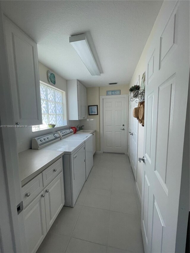 kitchen featuring light tile patterned flooring, white cabinets, washer and dryer, and a textured ceiling