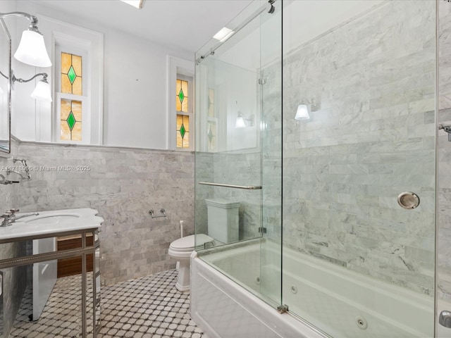 full bathroom featuring bath / shower combo with glass door, sink, tile walls, and toilet