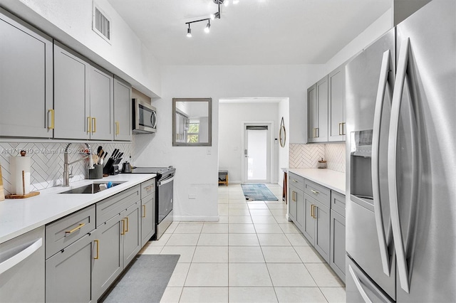 kitchen with gray cabinetry, sink, backsplash, light tile patterned floors, and appliances with stainless steel finishes