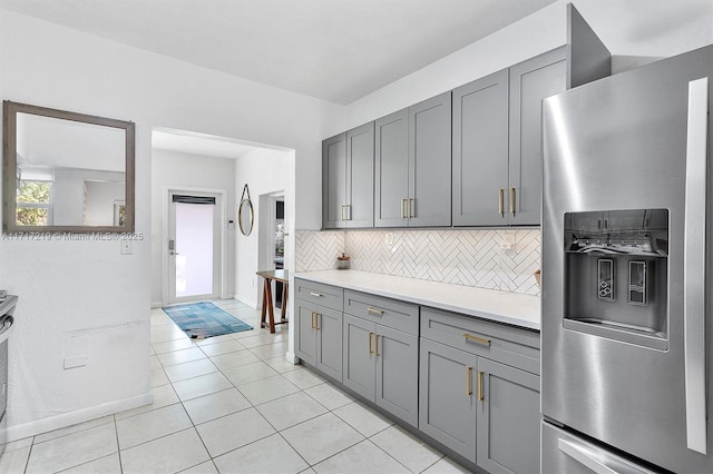 kitchen with gray cabinets, stainless steel fridge, light tile patterned floors, and backsplash