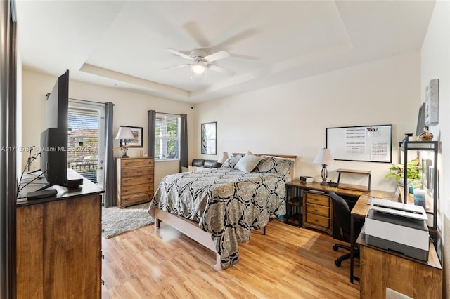 bedroom featuring access to exterior, a tray ceiling, light hardwood / wood-style flooring, and ceiling fan