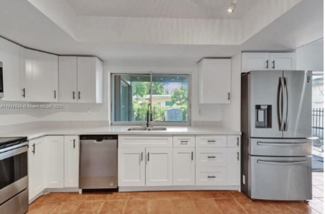 kitchen featuring a raised ceiling, white cabinetry, sink, and appliances with stainless steel finishes