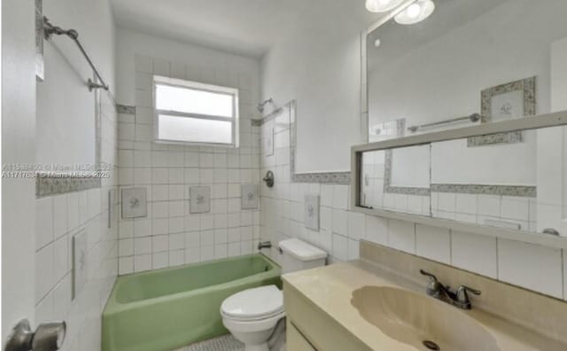 full bathroom featuring tiled shower / bath, vanity, toilet, and tile walls