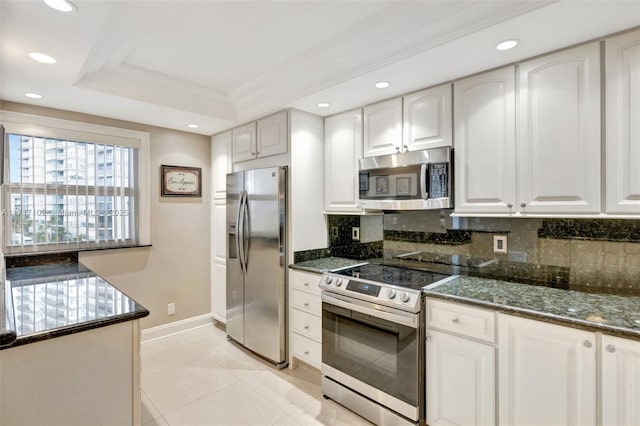 kitchen with dark stone countertops, ornamental molding, a tray ceiling, white cabinetry, and stainless steel appliances