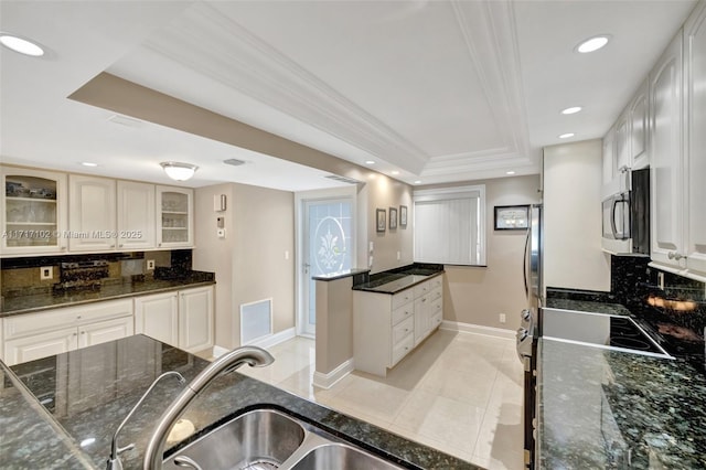 kitchen with decorative backsplash, light tile patterned floors, a tray ceiling, and dark stone counters