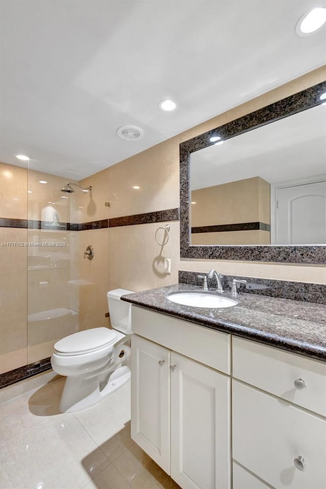 bathroom featuring vanity, tile patterned floors, toilet, tile walls, and a tile shower