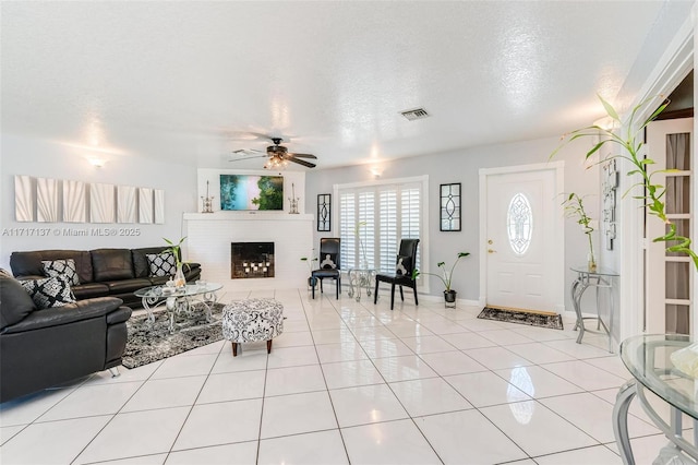 living room with ceiling fan, a fireplace, light tile patterned floors, and a textured ceiling