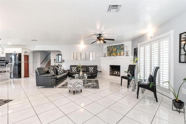 tiled living room featuring a fireplace, a textured ceiling, and ceiling fan