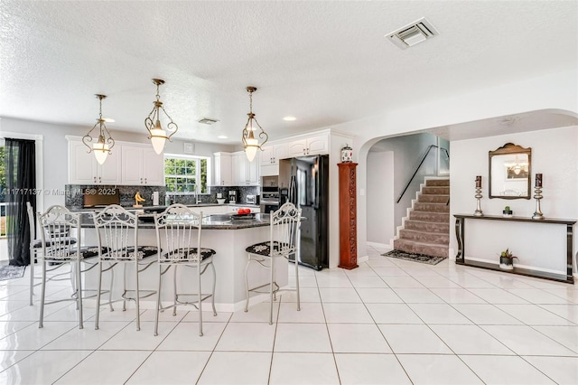 kitchen featuring dark stone countertops, black fridge, white cabinets, and hanging light fixtures