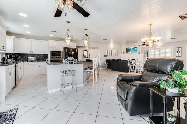 kitchen with white cabinetry, built in microwave, a center island, black fridge, and decorative light fixtures