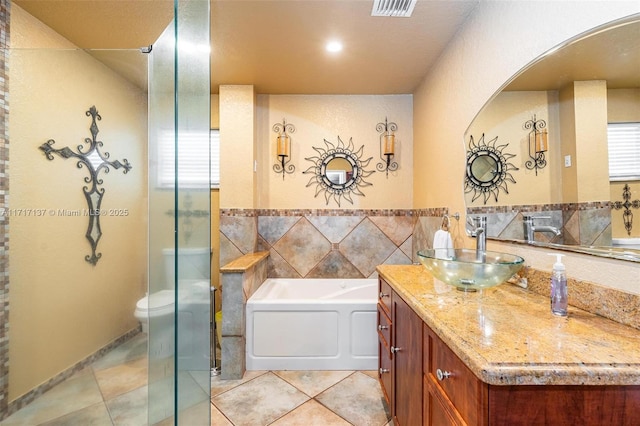 bathroom with a tub to relax in, vanity, tile walls, tile patterned flooring, and toilet