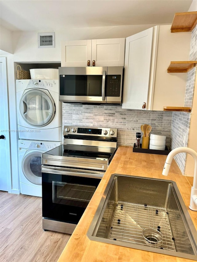 kitchen with stacked washer / dryer, white cabinets, wooden counters, and appliances with stainless steel finishes