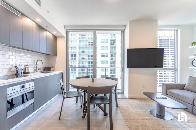 kitchen with black electric stovetop, tasteful backsplash, gray cabinetry, sink, and oven