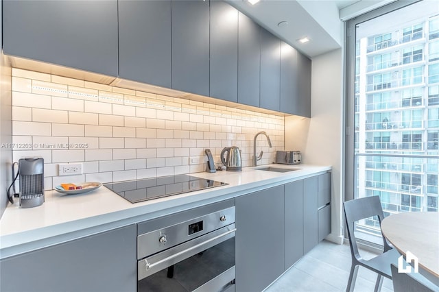 kitchen with backsplash, oven, sink, black electric cooktop, and light tile patterned flooring