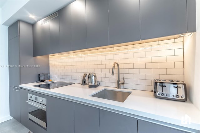 kitchen with backsplash, black electric cooktop, sink, and oven