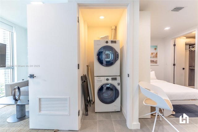 clothes washing area featuring stacked washer and dryer, light tile patterned floors, and plenty of natural light