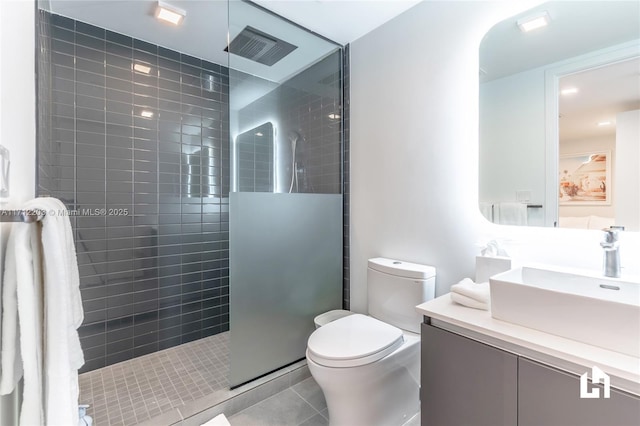 bathroom featuring toilet, a tile shower, vanity, and tile patterned floors