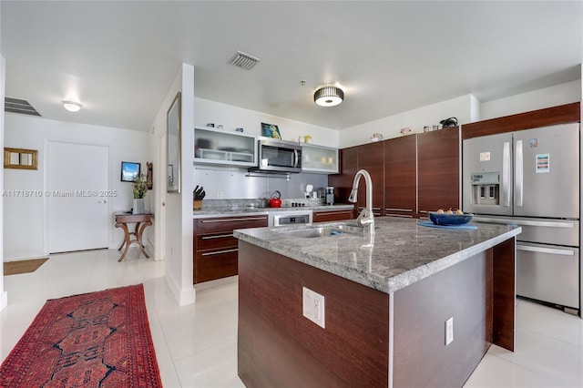 kitchen featuring dark brown cabinetry, appliances with stainless steel finishes, an island with sink, sink, and light tile patterned floors