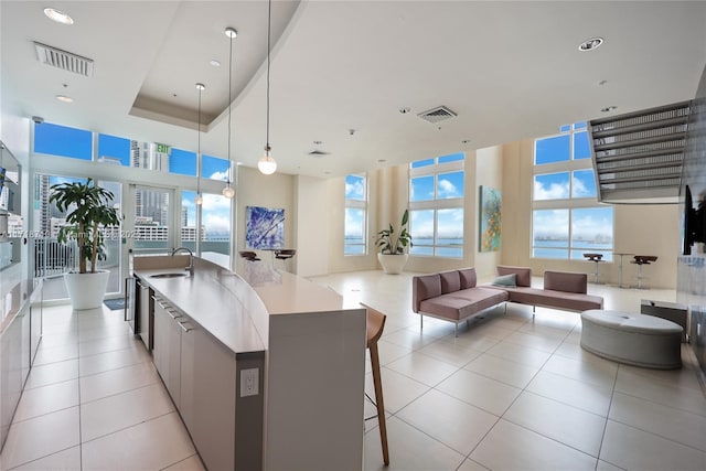 kitchen with a spacious island, decorative light fixtures, sink, a raised ceiling, and light tile patterned flooring