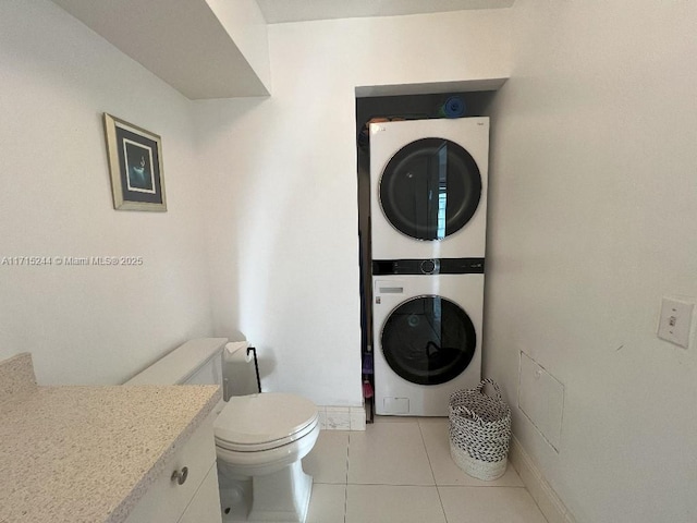 bathroom featuring toilet, vanity, stacked washing maching and dryer, and tile patterned floors