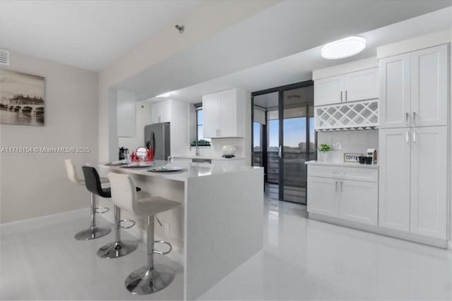 kitchen with white cabinets, a breakfast bar, stainless steel fridge with ice dispenser, and kitchen peninsula