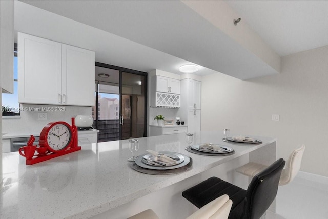 kitchen featuring a kitchen breakfast bar, white cabinetry, and light stone countertops