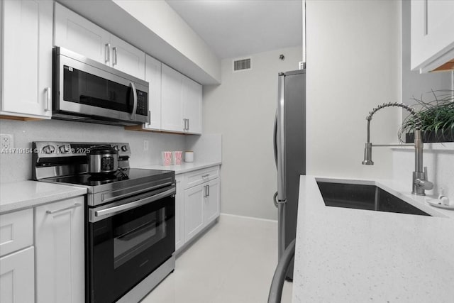 kitchen featuring sink, light stone countertops, tasteful backsplash, white cabinetry, and stainless steel appliances