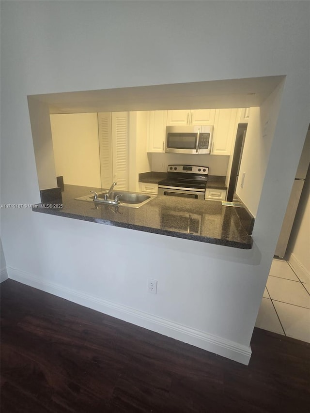 kitchen with white cabinetry, sink, stainless steel appliances, kitchen peninsula, and dark stone countertops