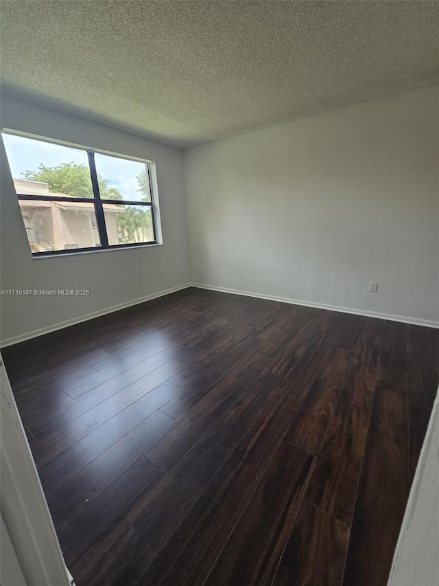 spare room with a textured ceiling and dark hardwood / wood-style floors