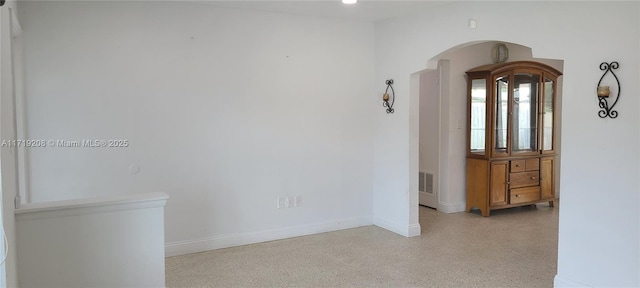 empty room featuring light speckled floor, arched walkways, visible vents, and baseboards