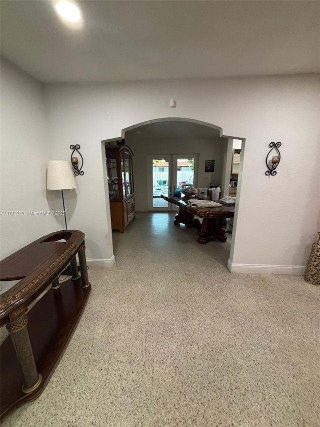 hall featuring arched walkways, french doors, baseboards, and speckled floor