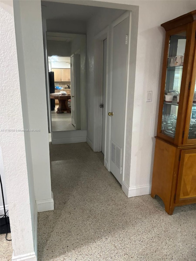 hall featuring light speckled floor, visible vents, and baseboards