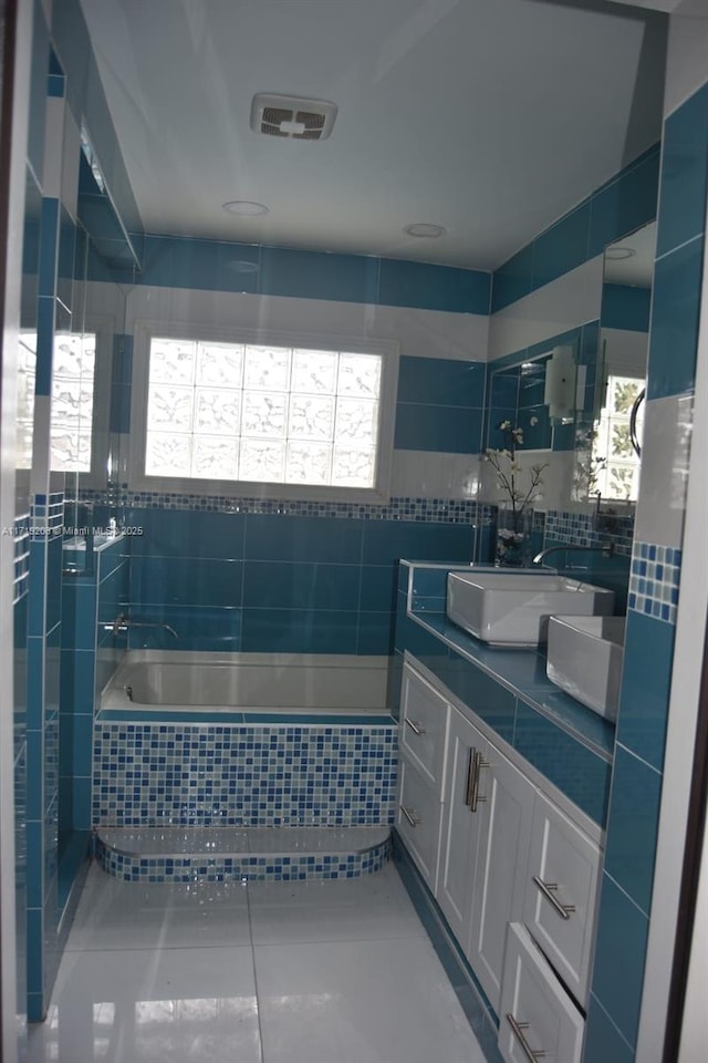 bathroom featuring tile walls, visible vents, vanity, tiled tub, and tile patterned floors