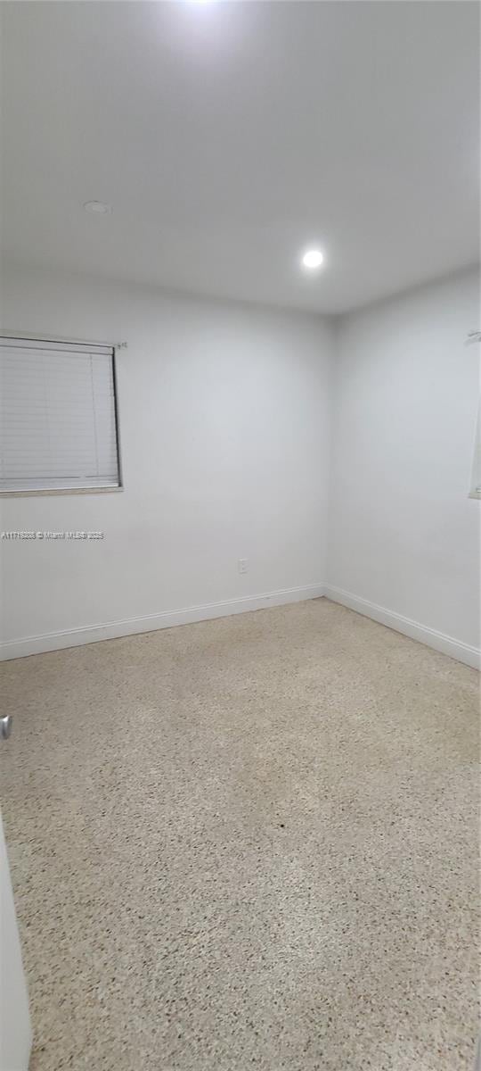 spare room featuring speckled floor, recessed lighting, and baseboards