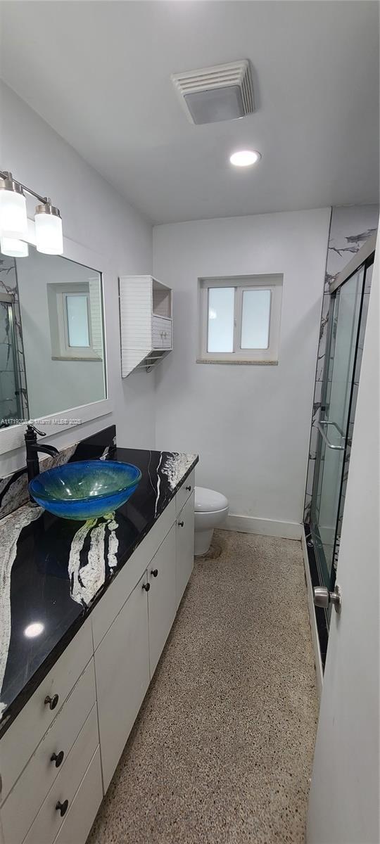 bathroom with visible vents, toilet, a shower stall, vanity, and speckled floor