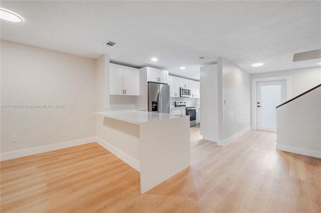 kitchen with light hardwood / wood-style floors, kitchen peninsula, white cabinets, and appliances with stainless steel finishes