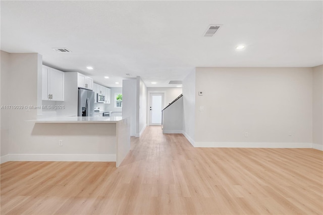 kitchen featuring appliances with stainless steel finishes, kitchen peninsula, light wood-type flooring, and white cabinets