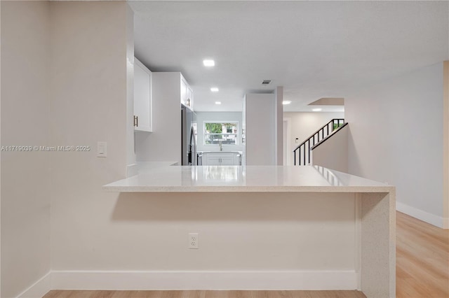 kitchen featuring white cabinetry, stainless steel fridge, kitchen peninsula, and light hardwood / wood-style flooring